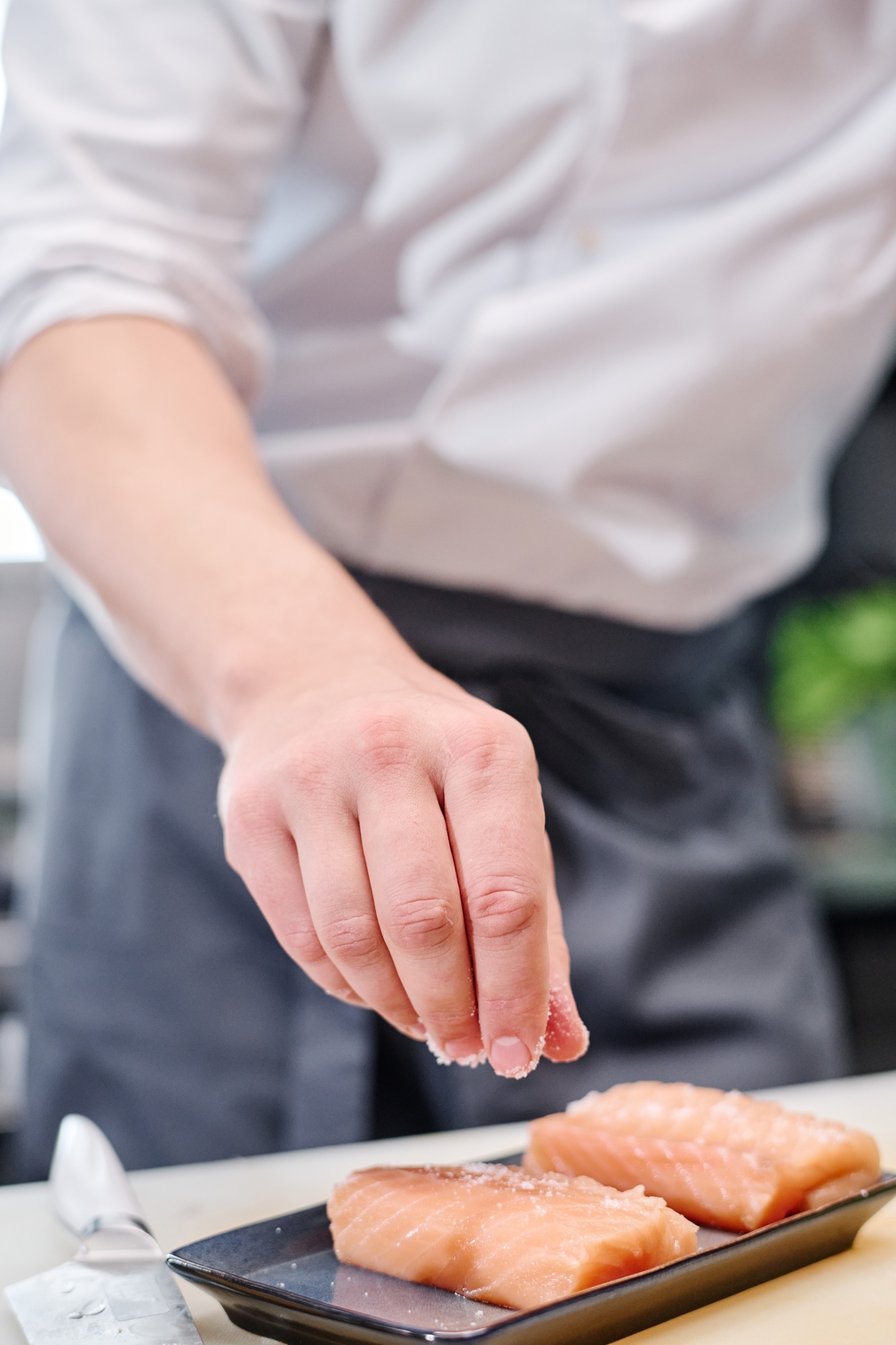 Chef salting salmon fish in kitchen