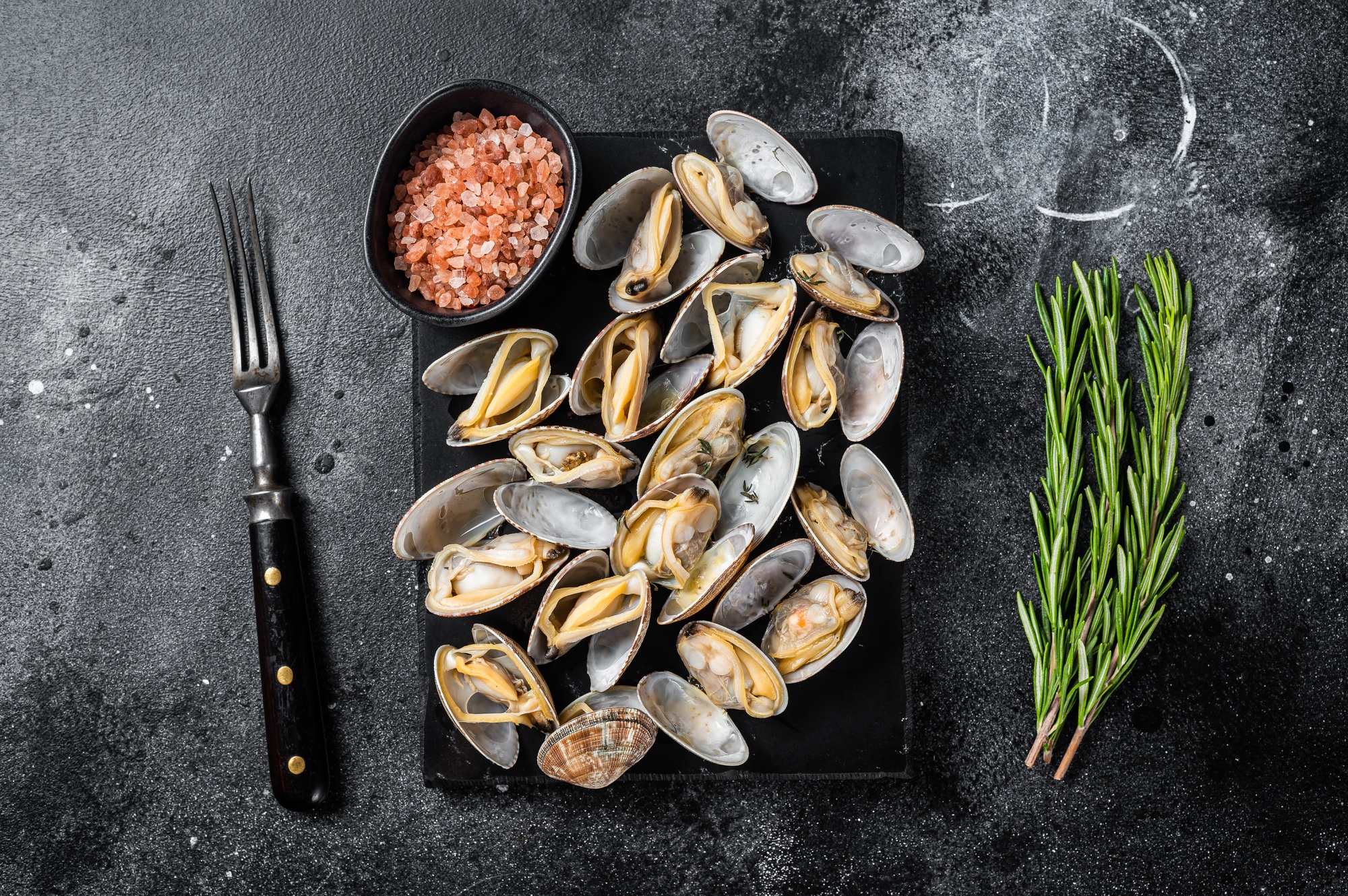 Steamed shellfish Clams with garlic and herbs. Black background. Top view